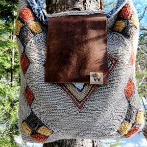 May include: A gray knitted tote bag with a brown leather flap and a metal tag with the letter "W". The bag has a geometric pattern in orange, yellow, and black.