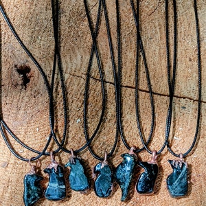 May include: Eight black necklaces with green stone pendants in various shapes. The necklaces are displayed on a wooden surface.