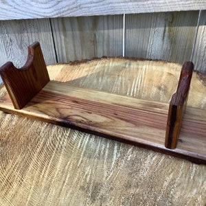 May include: A wooden stand with two upright supports and a flat base. The stand is made of light and dark brown wood and has a natural finish.