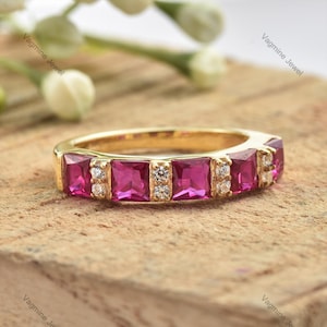 May include: A gold band ring with a row of pink square-shaped gemstones and smaller clear round gemstones.