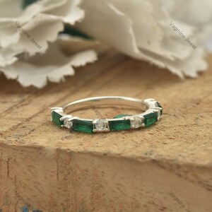 May include: A silver band ring with a row of emerald green and clear square-shaped gemstones.
