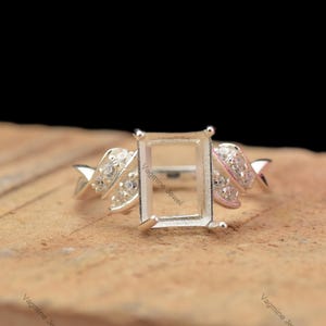 May include: Silver ring setting with a rectangular empty space for a gemstone. The ring has a twisted band with small clear stones.