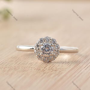 May include: A silver ring with a round, clear center stone surrounded by a halo of smaller stones.