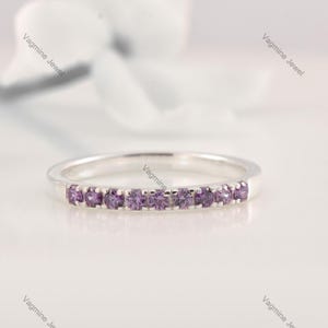 Può includere: Un delicato anello a fascia d'argento con una fila di piccole pietre preziose viola.