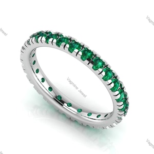 Può includere: Un anello a fascia d'argento con una fila di pietre preziose verde smeraldo incastonate attorno all'intera fascia.