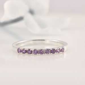 Peut inclure: Une bague en argent avec une rangée de petites pierres précieuses violettes.