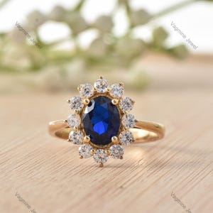 Op de afbeelding: Een gouden ring met een grote ovale blauwe saffier omringd door een halo van kleinere witte diamanten.