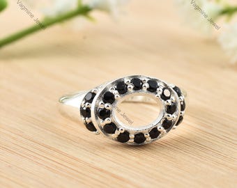 Puede incluir: Un anillo de plata con un engaste ovalado rodeado de piedras preciosas negras. El anillo está sobre una superficie de madera.