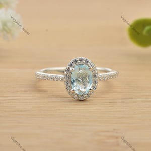 May include: A silver ring featuring a light blue oval gemstone set within a halo of smaller clear gemstones.