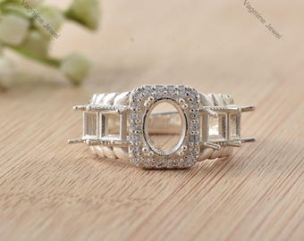 Puede incluir: Un anillo de plata con un engaste cuadrado con una piedra central redonda. El anillo está engastado con pequeños diamantes alrededor de la piedra central y en la banda.
