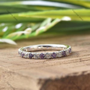May include: A silver band ring with a row of small, round, clear and purple gemstones.