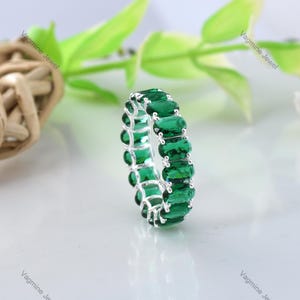 May include: A silver band ring with a row of emerald green oval-shaped gemstones.