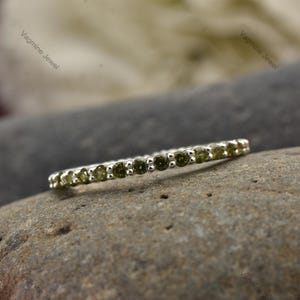 以下が含まれることがあります： 小さな丸い緑色の宝石が並んだ、繊細な銀のバンドリングです。