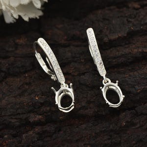 May include: A pair of silver dangle earrings with a clear crystal pave design and a bezel setting for a stone. The earrings have a lever back closure.