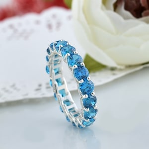 May include: A silver band ring with a row of blue gemstones. The ring is set with round, faceted stones that create a sparkling effect.