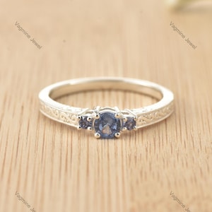 Può includere: Un anello d'argento con tre pietre preziose blu. L'anello ha un design intricato sulla fascia.