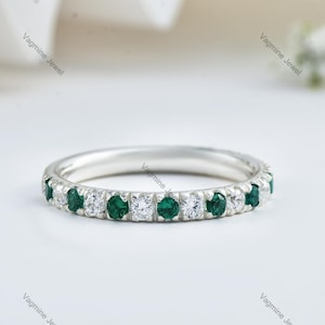 May include: A silver band ring with a row of alternating emerald green and clear round stones.