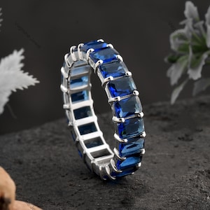 May include: A silver band ring with a row of blue emerald-cut gemstones. The ring is set with a total of 10 stones.