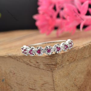 May include: A delicate silver band ring with a row of small, round, pink gemstones set in a scalloped design.