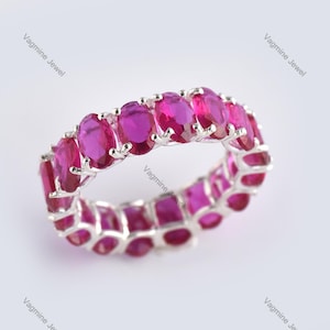 May include: A silver ring with a band of oval-shaped pink gemstones. The ring is set with a row of pink stones around the entire band.