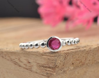 Puede incluir: Un anillo de plata con una banda de cuentas y una sola piedra preciosa rosa redonda en el centro.