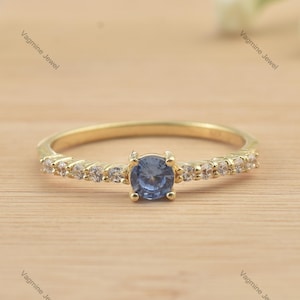 Peut inclure: Une délicate bague en or avec une seule pierre précieuse bleue entourée de petites pierres précieuses claires.