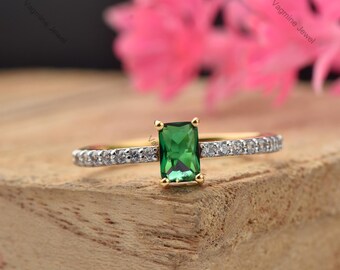 Puede incluir: Un anillo de oro con una esmeralda verde y una banda de pequeños diamantes.