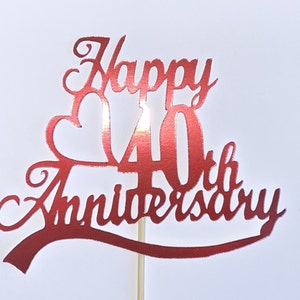 May include: A red cake topper with the words "Happy 40th Anniversary" in a decorative font. The topper is attached to a wooden stick for insertion into a cake. Ideal for celebrating a 40th wedding anniversary.