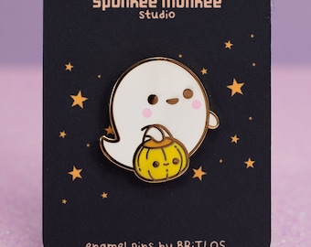 Op de afbeelding: Een Halloween-emaille pin met een schattig wit spookje dat een gele pompoen vasthoudt. De pin zit op een zwarte kaart met de tekst "SPECKLES TRICK OR TREAT" en "spunkee monkee studio".