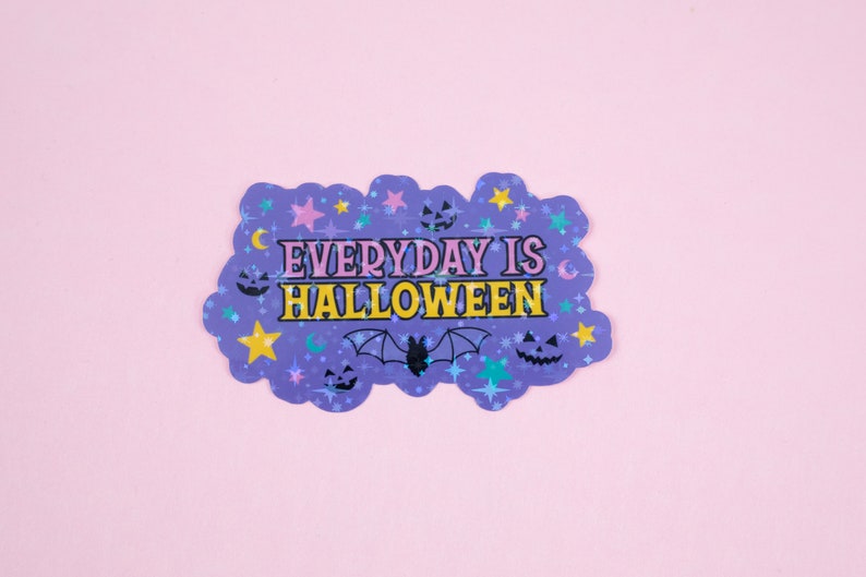 Puede incluir: Pegatina morada con un dise&ntilde;o brillante que presenta estrellas, lunas, murci&eacute;lagos y calabazas. El texto dice "EVERYDAY IS HALLOWEEN" en letras amarillas y rosas.