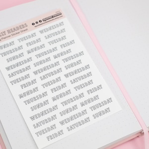 May include: A planner sticker sheet with weekly headers, featuring the days of the week in a repeating pattern. The stickers are in a sans-serif font with a black outline. The sheet is on a white notebook with a pink cover.