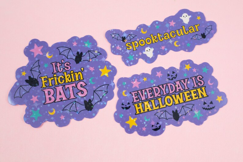 Puede incluir: Tres pegatinas hologr&aacute;ficas moradas con purpurina y estrellas. La primera pegatina dice "It's Frickin' Bats" en letras rosas y amarillas. La segunda pegatina dice "Spooktacular" en letras amarillas. La tercera pegatina dice "Everyday is Halloween" en letras rosas y amarillas.