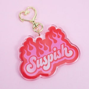 Pode incluir: Um chaveiro de acr&iacute;lico vermelho e rosa com um design de chama e a palavra "Suspish" em letras brancas.