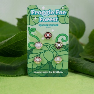 K&ouml;nnte beinhalten: Satz mit vier Emaille-Pins mit verschiedenen farbigen Pilzdesigns. Die Pins befinden sich auf einer Karte mit dem Text "Froggie Fae Forest" und "enamel pins by BritLos."