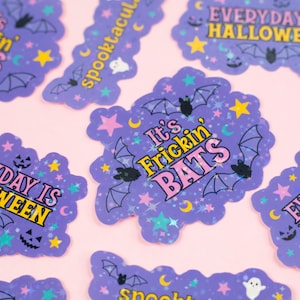 Puede incluir: Pegatinas de Halloween moradas y amarillas con purpurina y varios dise&ntilde;os. Las pegatinas presentan murci&eacute;lagos, estrellas, lunas y el texto "It's Frickin' Bats" y "Everyday is Halloween".