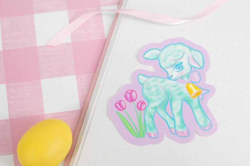May include: A pastel green lamb sticker with a pink bow and a gold bell. The lamb is standing on a purple background with pink tulips.