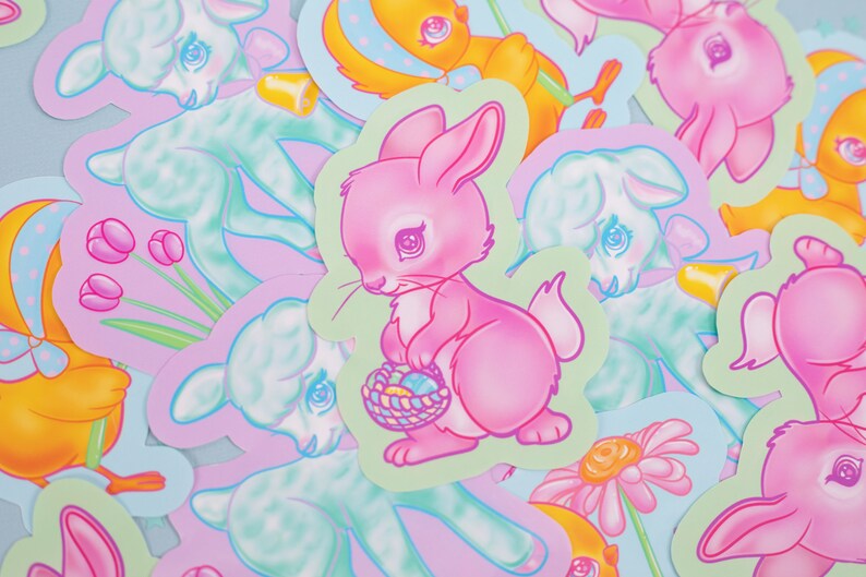 May include: A collection of pastel-colored Easter stickers featuring a pink bunny holding a basket of eggs, a blue lamb, and a yellow chick. The stickers are on a light blue background.
