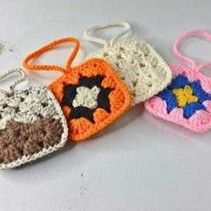 May include: Four colorful, crocheted granny square pouches with loop handles. The pouches are in shades of beige, brown, orange, cream, pink, blue, and yellow. The granny squares are arranged in a row, showcasing the handmade details.