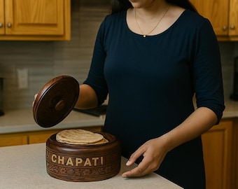 Puede incluir: Una caja de chapati de madera marrón oscuro con tapa, llena de pan plano. La caja tiene la palabra "CHAPATI" tallada en el lateral. Se levanta la tapa, revelando el contenido. La caja está sobre una encimera en una cocina.