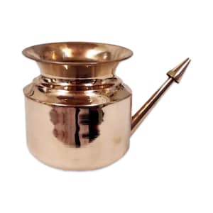 May include: A copper-colored neti pot with a rounded base, a wide, flared rim, and a long, angled spout. The pot has a smooth, reflective surface and is designed for nasal irrigation. The spout has a pointed tip.