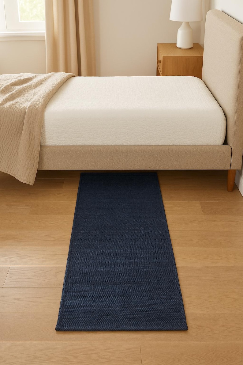 K&ouml;nnte beinhalten: Ein rechteckiger, marineblauer Teppich liegt auf einem hellen Holzboden unter einem Bett. Der Teppich hat eine strukturierte Oberfl&auml;che und befindet sich vor dem Bett. Das Bett hat ein beiges Kopfteil und eine wei&szlig;e Matratze.