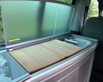 May include: A white van with a built-in kitchen counter. The counter has a sink, two wooden cutting boards, and a gray cabinet.