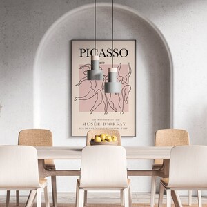 Puede incluir: Un comedor con una mesa blanca y seis sillas. La mesa est&aacute; puesta con un cuenco de limones y un jarr&oacute;n de hierba de la pampa seca. Un p&oacute;ster con el texto "PICASSO" y "MUSEE D'ORSAY" cuelga de la pared.