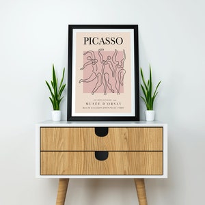 Puede incluir: Una impresi&oacute;n enmarcada en negro con un fondo rosa y un dibujo de l&iacute;nea negra de bailarines. La impresi&oacute;n tiene el texto "PICASSO" y "MUSEE D'ORSAY" en negro.