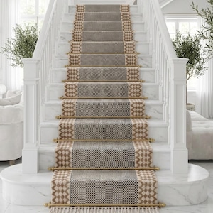 Puede incluir: Una escalera con una alfombra de pasillo estampada en gris y beige. La alfombra tiene un diseño geométrico y está bordeada por un patrón de diamantes beige y marrón. Las escaleras son de mármol blanco con barras y borlas de latón.