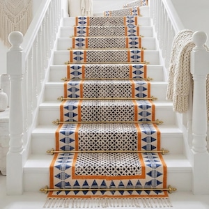 May include: Staircase with white risers and treads, featuring patterned stair runners in black, orange, and blue geometric designs. Brass rods secure the runners. The overall aesthetic is a blend of modern and bohemian styles.