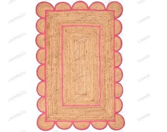 May include: A natural fiber rug with a pink border and scalloped edges. The rug has a woven texture and a rectangular shape.