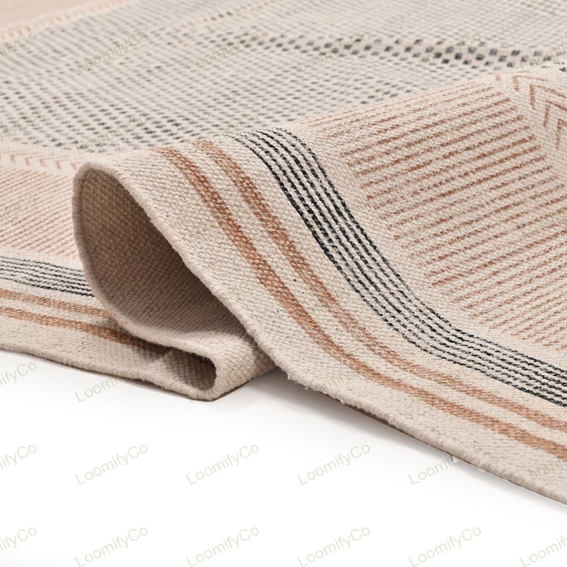 May include: Close-up of a beige and brown woven rug with black stripes. The rug has a textured surface and is folded over on itself.