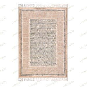 May include: A cream-colored rug with a black and white geometric pattern in the center. The rug has a brown and cream border with a fringe on all sides.