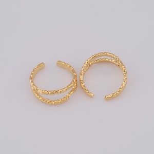 May include: Two gold-toned ear cuffs with a textured, beaded design. The cuffs are open and have a curved shape.